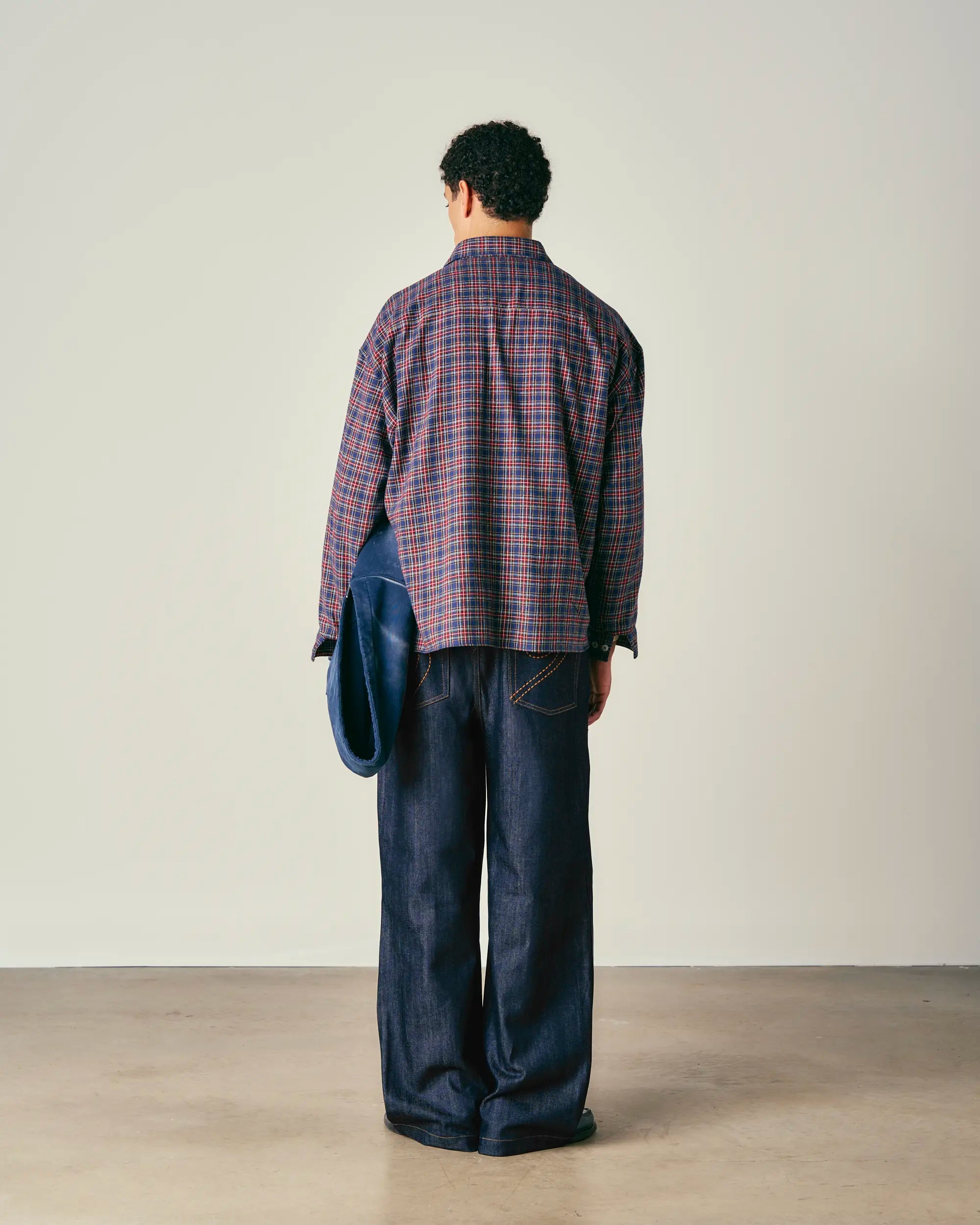 Person wearing a plaid shirt and dark jeans against a plain background