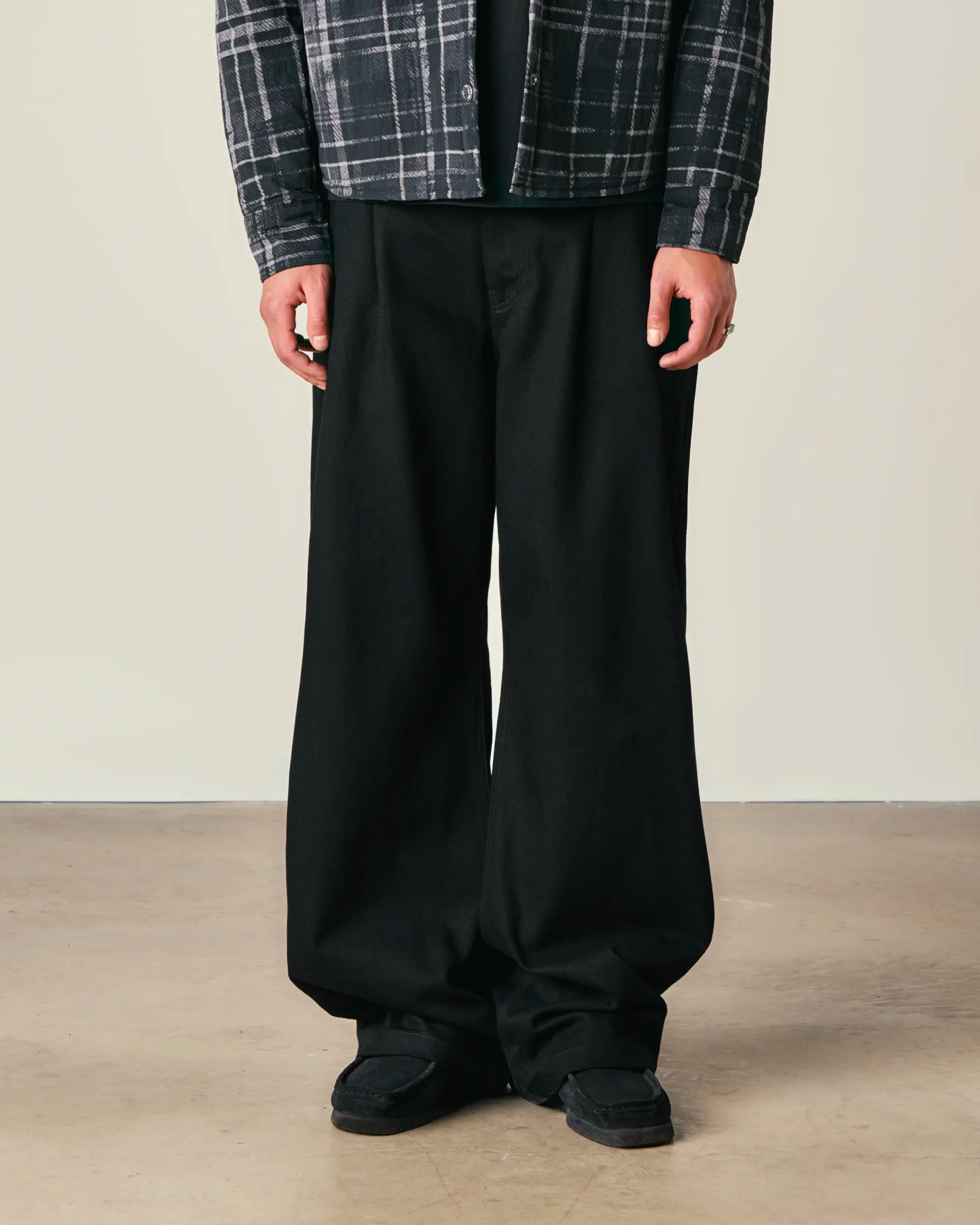 Person wearing black wide-leg pants with a plaid shirt on a neutral background