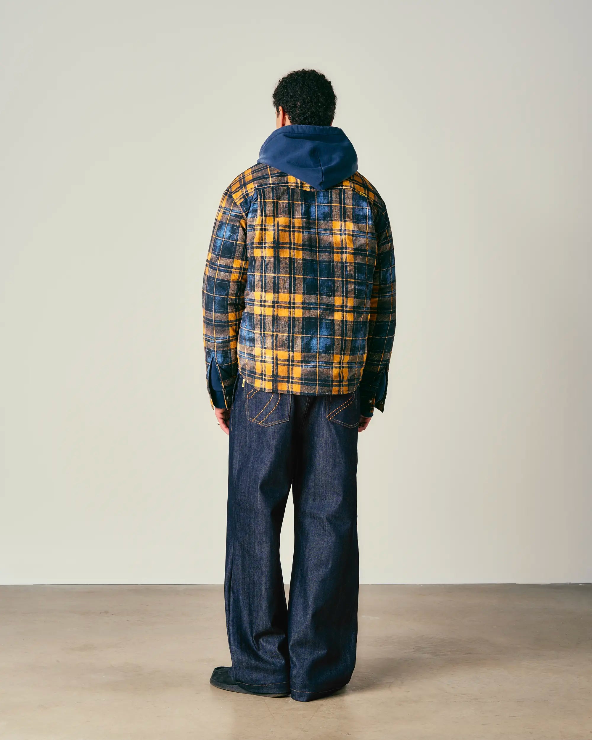 Person wearing a blue and yellow padded jacket with a hood, standing against a plain background.