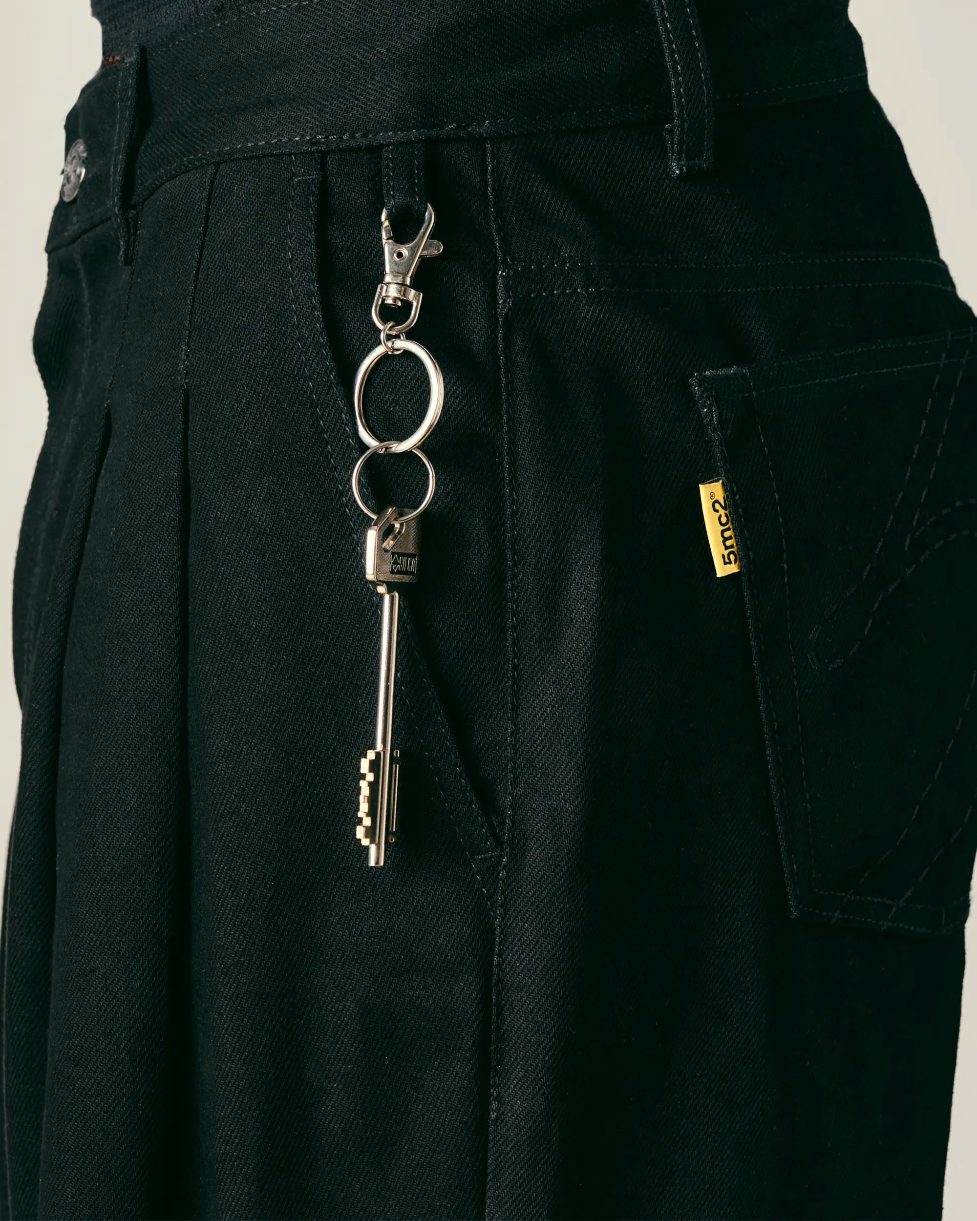 Keychain with keys attached to a black pants pocket on a neutral background