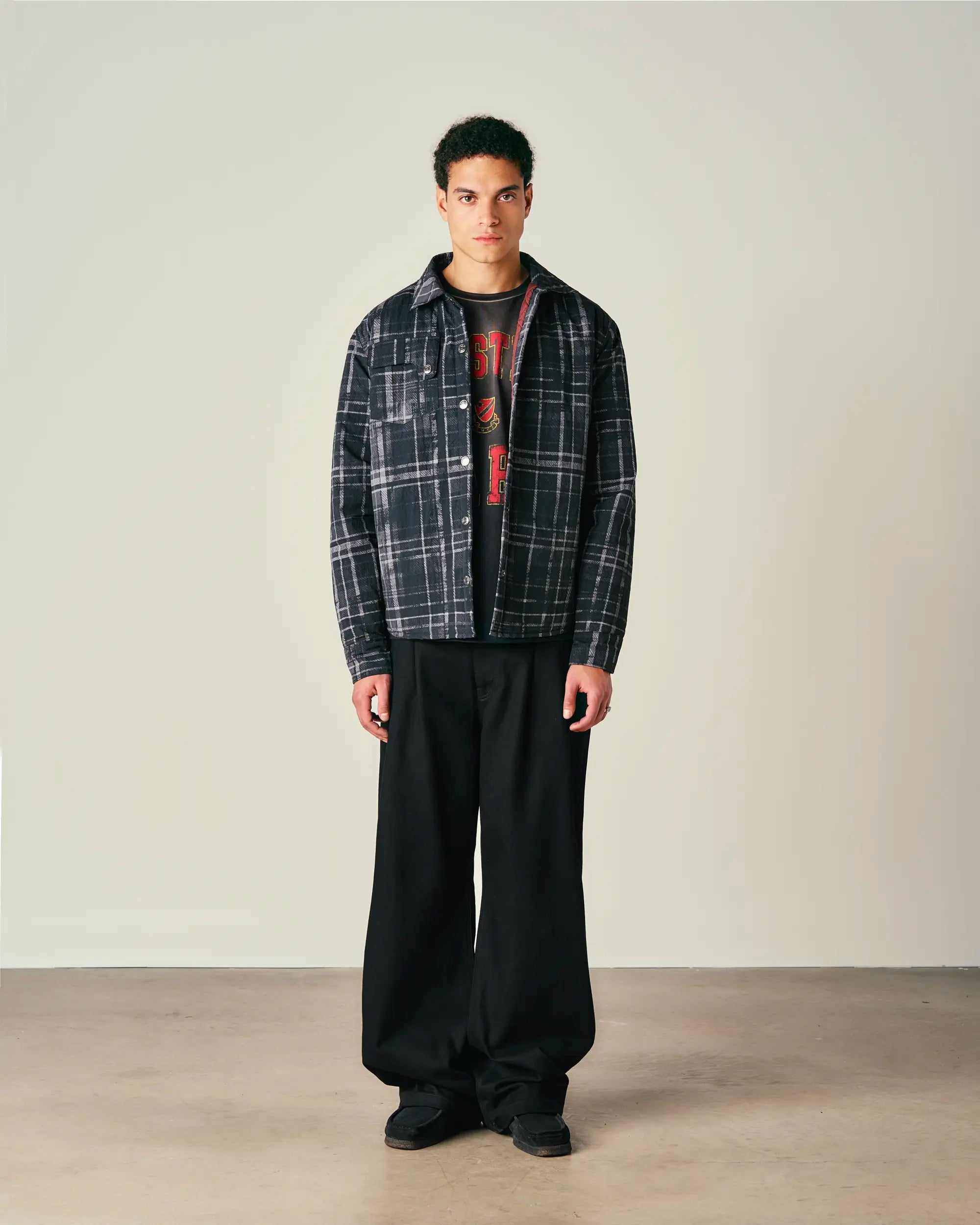 Person wearing a plaid jacket and black pants on a plain background