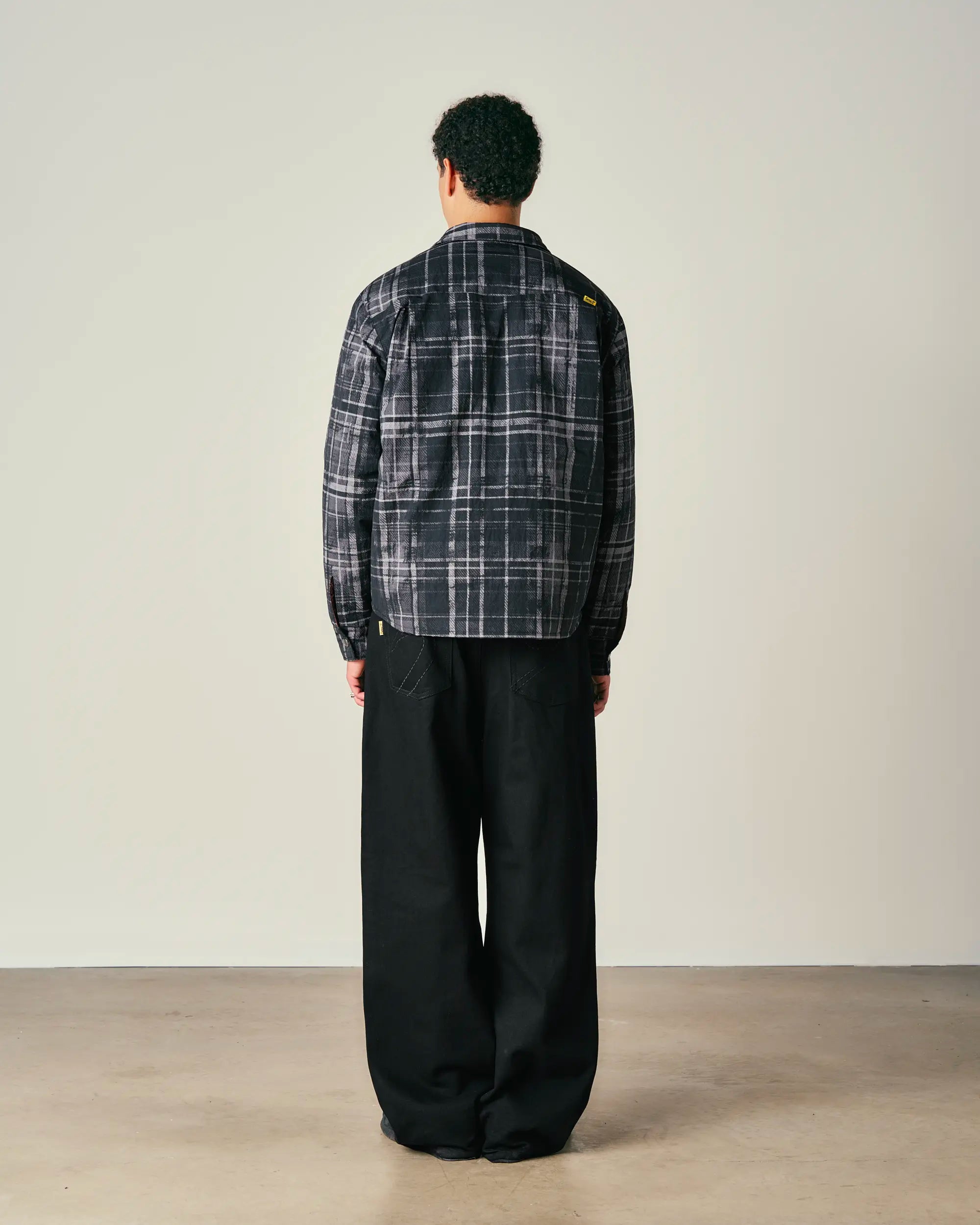 Person wearing a plaid shirt and black pants against a plain background