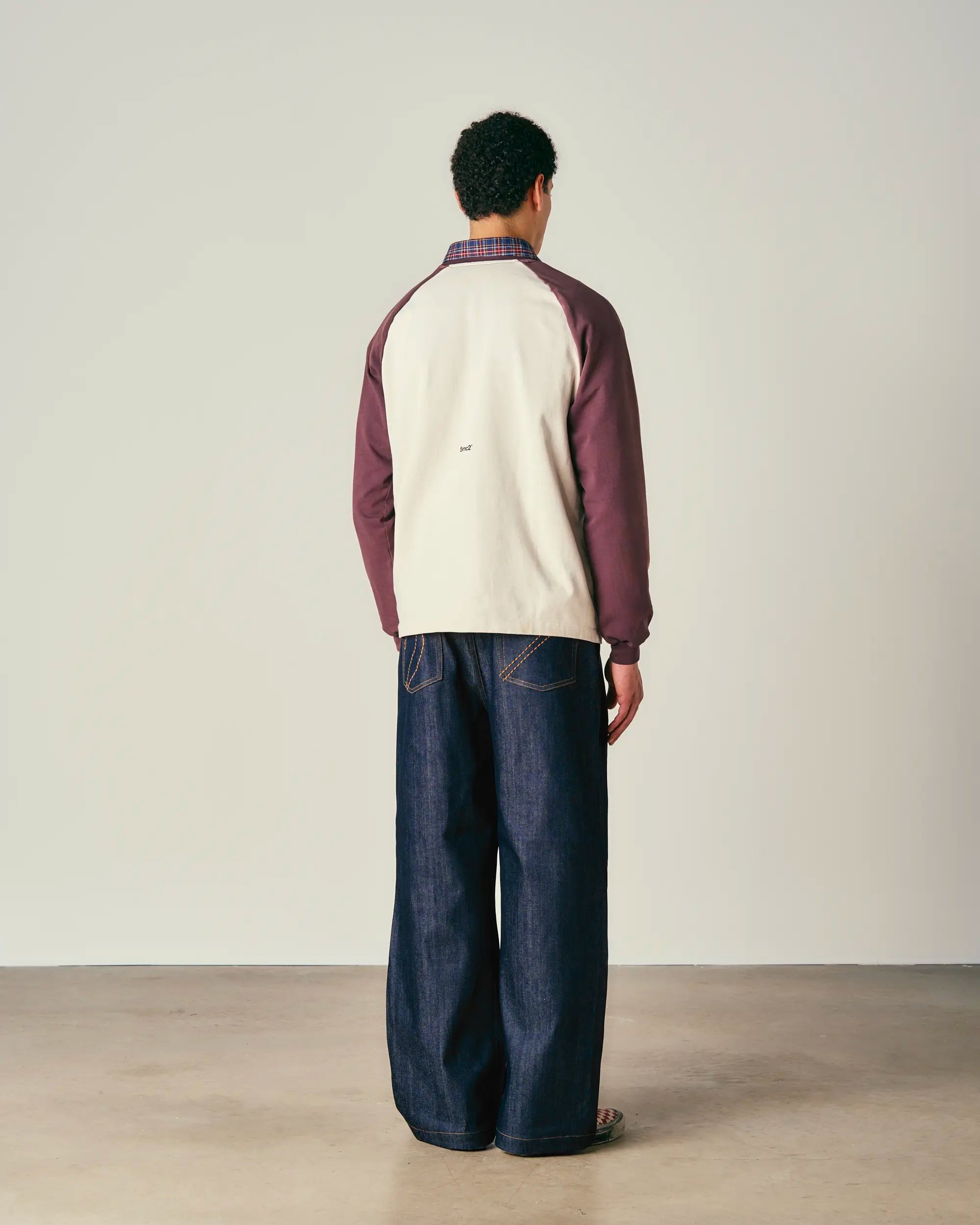 Person wearing a two-tone jacket and dark jeans standing against a plain background