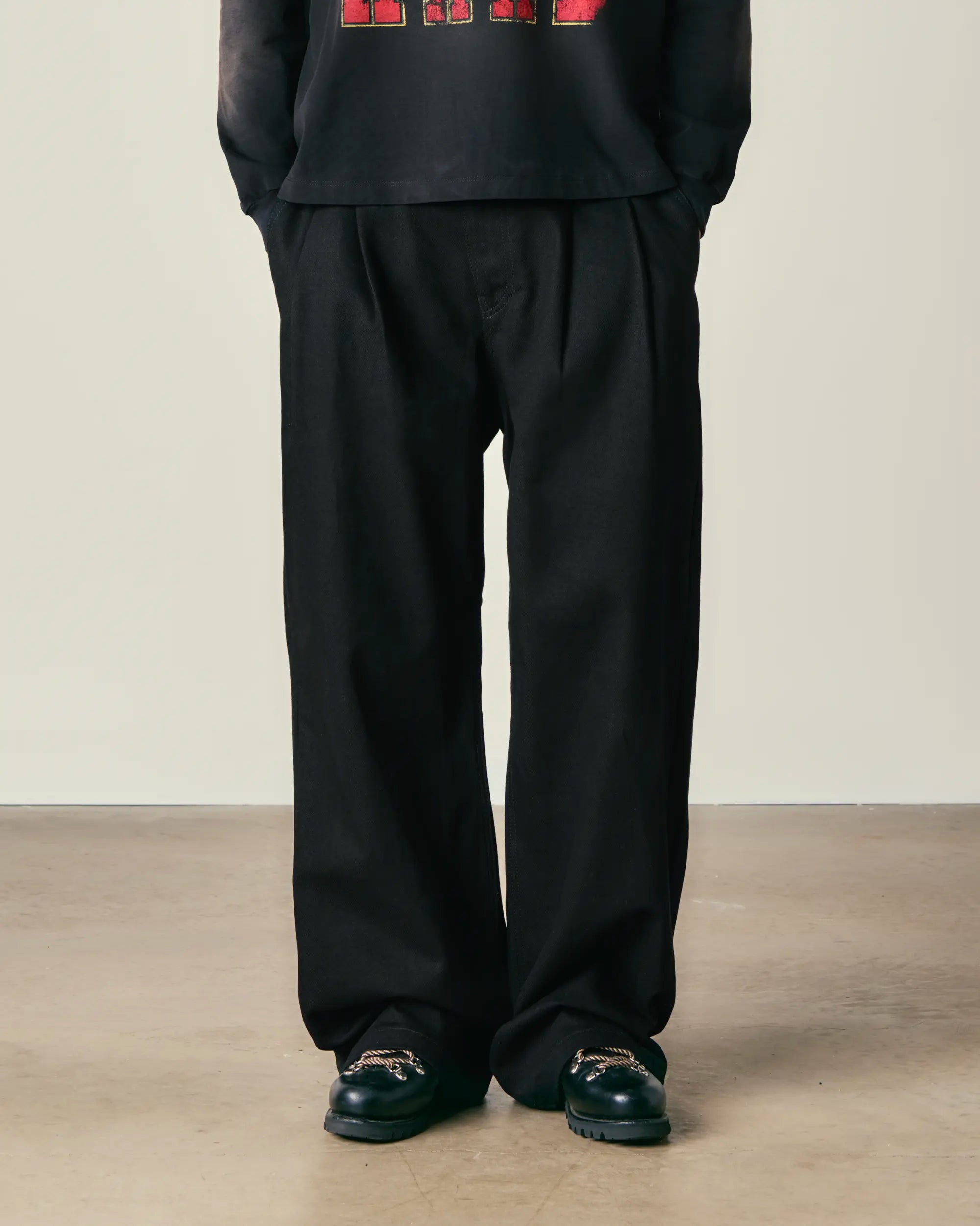 Person wearing a black outfit with wide-leg pants and black shoes on a plain background