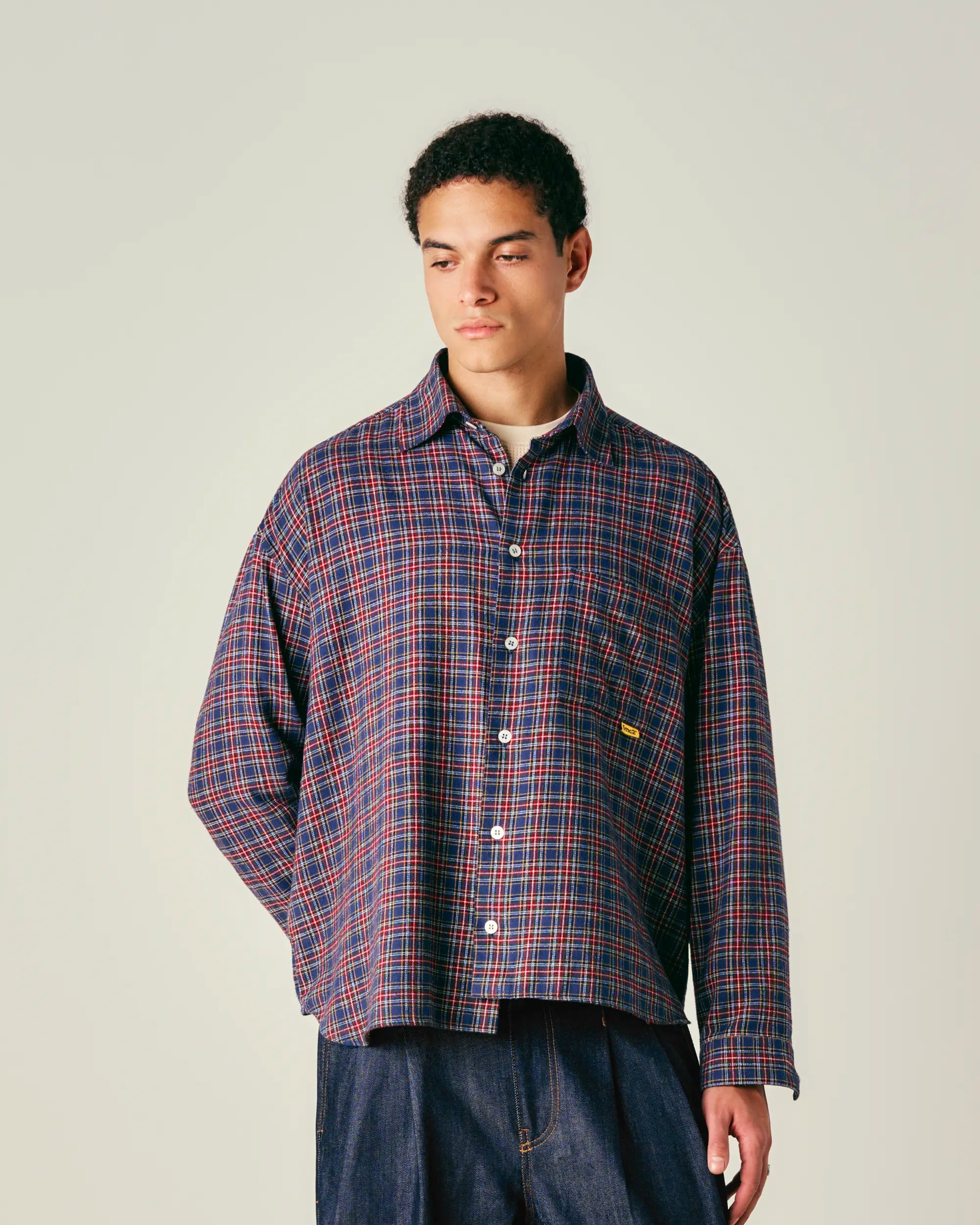 Person wearing a plaid shirt with a visible brand logo on a plain background